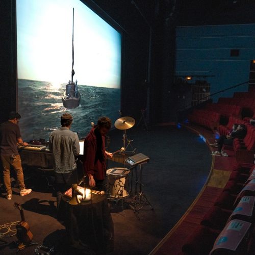 Le ciné-concert Machines à rêves : Des musiciens jouent devant un grand écran de cinéma qui diffuse des films à des familles et des enfants