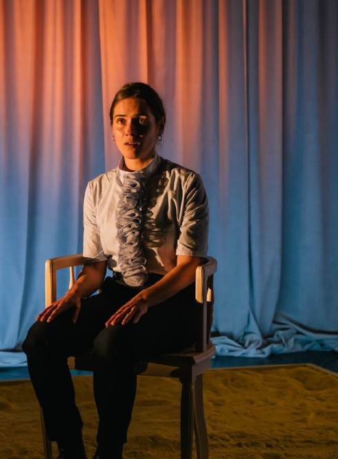 Papier peint jaune - Cie Paper Doll : Une femme assisse seule sur une chaise au milieu de la scène