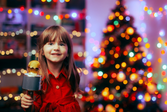Karaoké en famille : Une petite fille devant un sapin illuminé avec un micro
