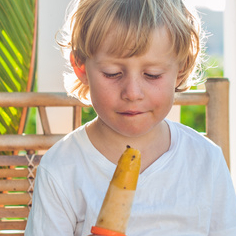 Cute little blond boy eating a homemade icecream sitting on a wooden chair