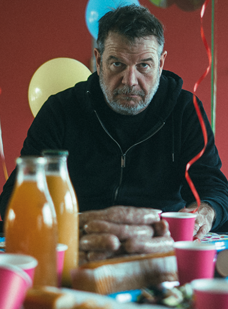 Rencontre avec Michel B : Un homme assis seul à table dans une salle des fêtes