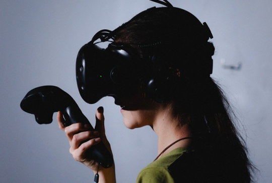 I-WAY : Une femme avec une manette dans une main et un casque de réalité virtuelle sur les yeux