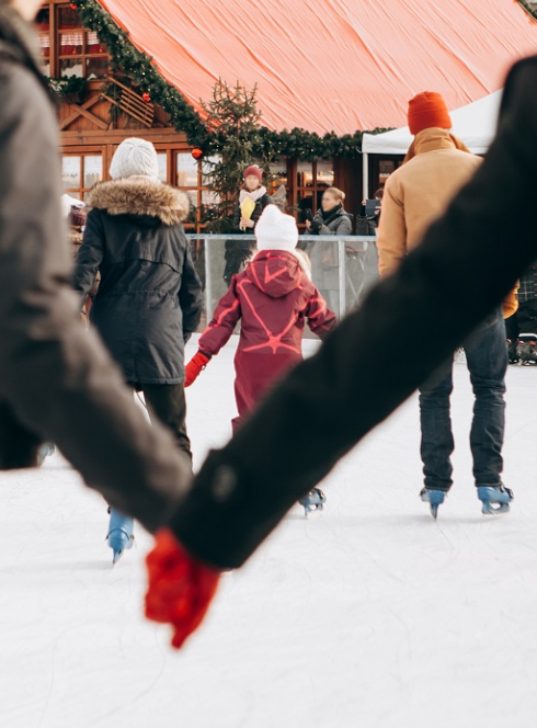Le top des sorties patinoire en famille : sur une patinoire, un couple se tient la main et des familles patinent