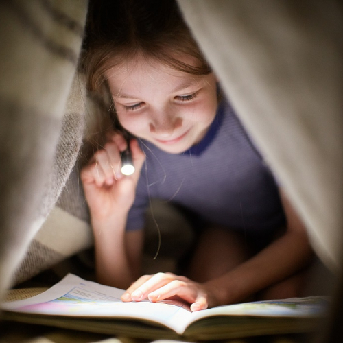 Les Nuits de la lecture : Une petite fille lit un livre sous un plaid avec une lampe torche