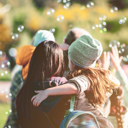 Top des festivals jeune public à ne pas rater en 2025 : Une petite fille dehors dans les bras de sa mère entourée de bulles de savon