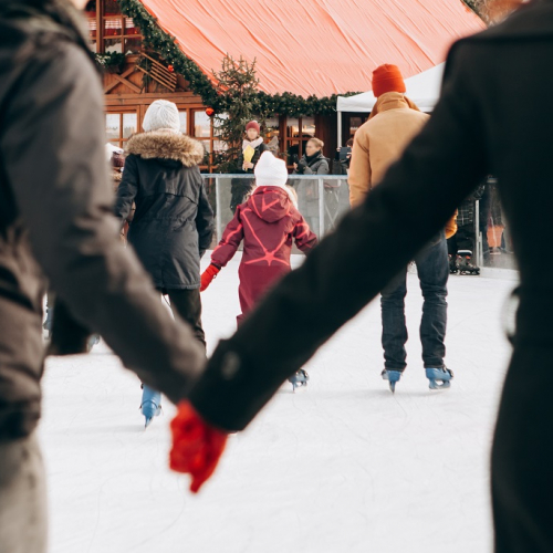 Le top des sorties patinoire en famille : sur une patinoire, un couple se tient la main et des familles patinent