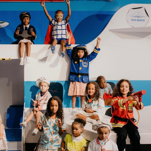 Palomano : Des enfants portent les tenues de diverses professions dans une salle qui ressemble à un aéroport