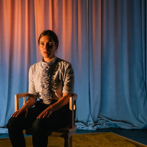 Papier peint jaune - Cie Paper Doll : Une femme assisse seule sur une chaise au milieu de la scène