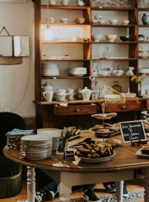 BrocCafé : Une table avec des gâteaux dessus au milieu d'objets de brocante