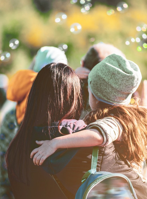 Top des festivals jeune public à ne pas rater en 2025 : Une petite fille dehors dans les bras de sa mère entourée de bulles de savon
