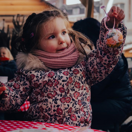 Marché de Noël de Lille et du Nord en 2024 : Une petite fille au marché de Noël tient une boule à accrocher au sapin