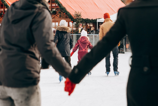 Le top des sorties patinoire en famille : sur une patinoire, un couple se tient la main et des familles patinent