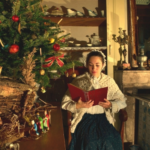 Noël d'antan au Musée de la Vie Rurale : Une dame en costumé d'époque fait la lecture à côté d'un sapin de Noël