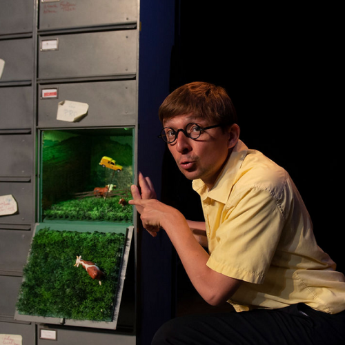 Léon - Cie Pocket Théâtre : un drôle de personnage à lunettes rondes et une petite maquette