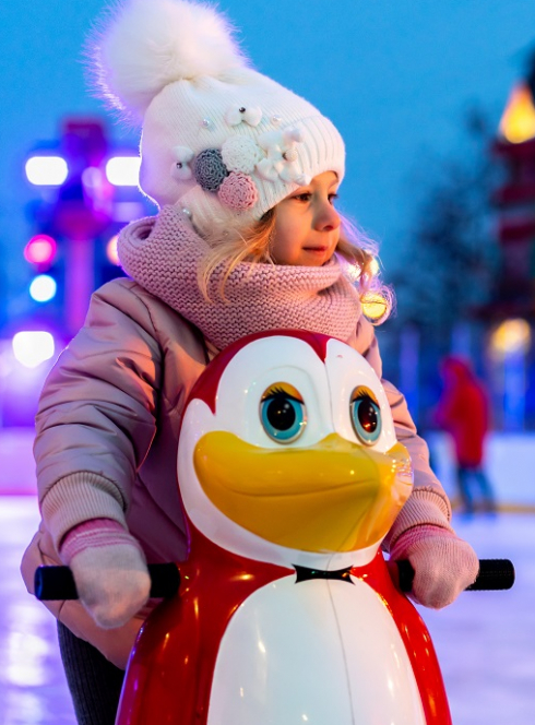 Patinoires : Une petite fille s'amuse sur la glace avec un pingouins pour l'aider