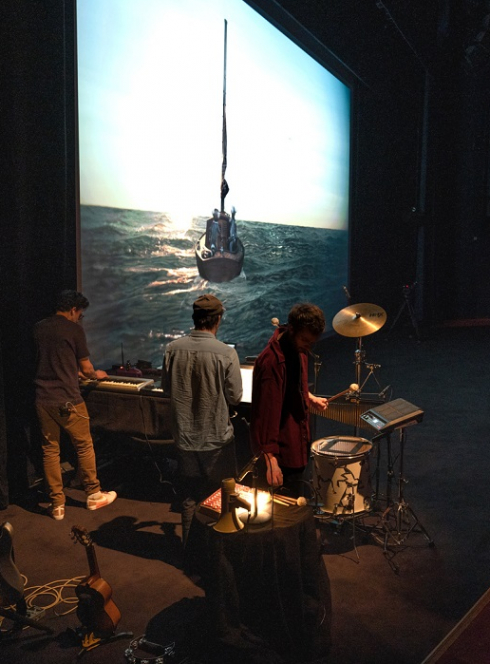 Le ciné-concert Machines à rêves : Des musiciens jouent devant un grand écran de cinéma qui diffuse des films à des familles et des enfants