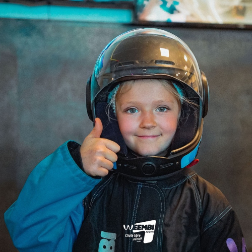 Weembi - chute libre indoor : Une petite fille équipée met son pouce en l'air