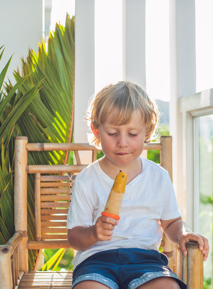 Cute little blond boy eating a homemade icecream sitting on a wooden chair