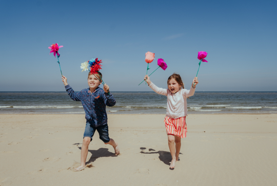Plage d'Ostende : Une petite fille et un petit garçon courent sur la plage, des fleurs en papier dans les mains