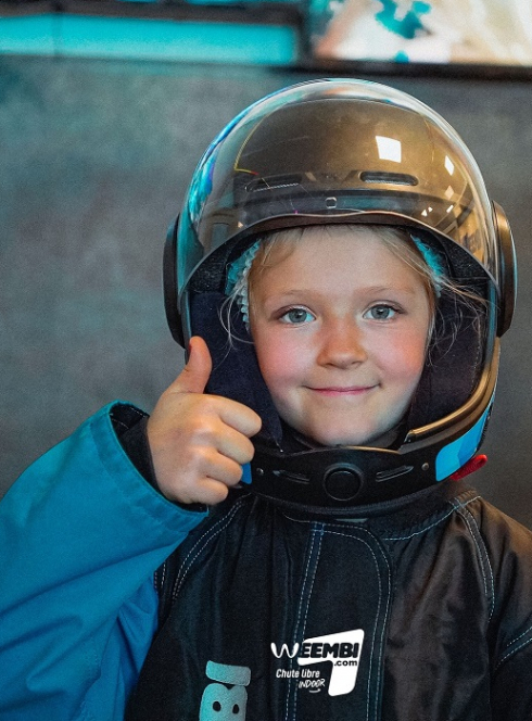 Weembi - chute libre indoor : Une petite fille équipée met son pouce en l'air